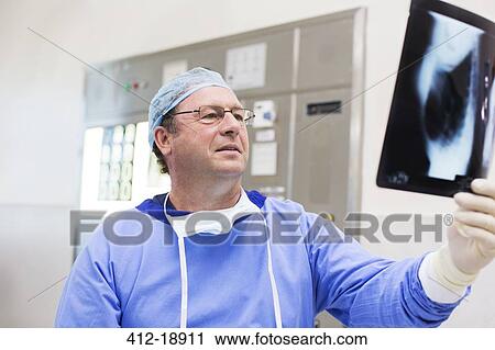 Stock Image - Doctor wearing surgical cap and gown looking at x-ray in operating theater. Fotosearch