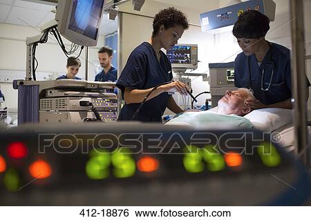 Stock Photograph - Doctors attending patient in intensive care unit, monitoring equipment in foreground. Fotosearch