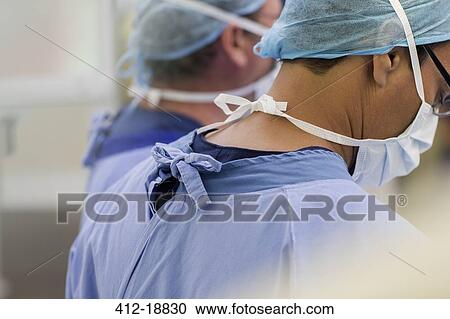 Stock Image - Doctors wearing surgical caps, masks and scrubs in operating theater. Fotosearch