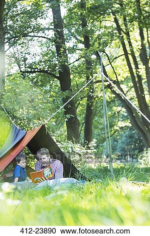 Stock Image - Father and son reading in camping tent. Fotosearch