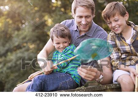 Stock Image - Father and sons fishing with net on dock. Fotosearch