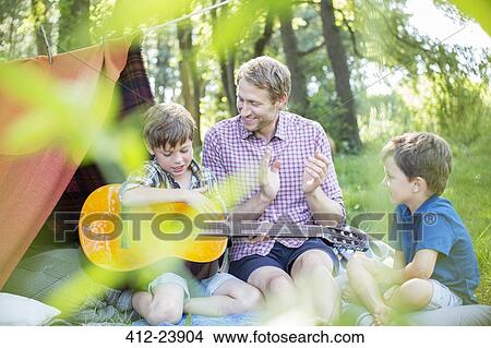 Picture - Father and sons playing guitar near camping tent. Fotosearch