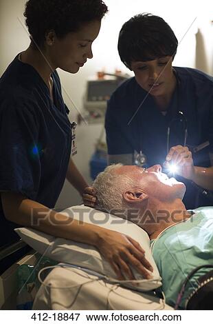 Stock Photo - Female doctor examining senior patient with flashlight in intensive care unit. Fotosearch