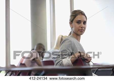 Picture - Female student looking at camera and sitting at desk during lecture. Fotosearch