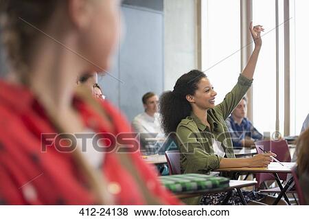 Stock Photo - Female student raising hand during lecture with other students in background. Fotosearch