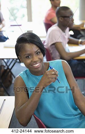 Female student smiling at camera during lecture with other students in background View Large Photo Image Picture - Female student smiling at camera during lecture with other students in background. Fotosearch