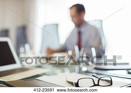 Stock Image - Glasses on conference table, businessman sitting in background. Fotosearch