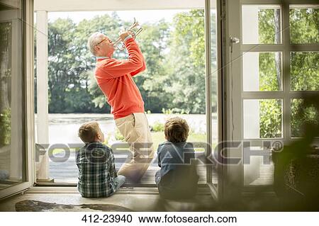 Stock Image - Grandfather playing trumpet for grandsons. Fotosearch