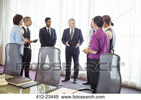 Stock Photo - Group of business people standing by window discussing in conference room. Fotosearch