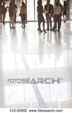 Stock Image - Group of business people standing in office, reflections in tiled floor. Fotosearch