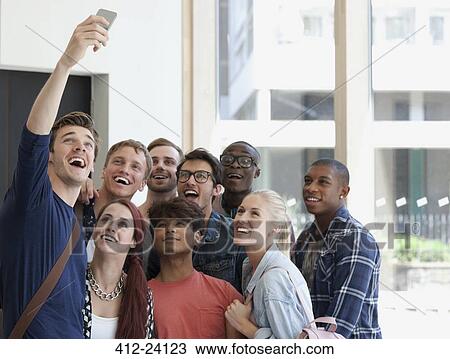 Stock Image - Group of laughing students taking selfie on corridor with large window in background. Fotosearch