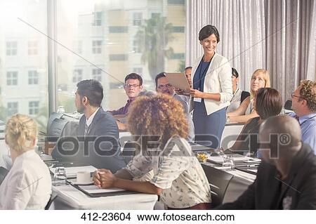 Picture - Group of people sitting at desks and listening to speaker. Fotosearch