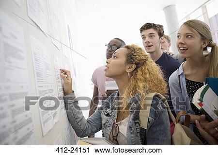 Stock Image - Group of students looking at information board and holding books at school. Fotosearch