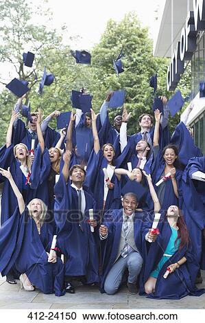 Stock Image - Group portrait of students in graduation gowns throwing mortarboards in the air. Fotosearch