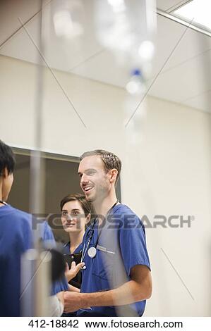 Stock Image - IV drip in front of doctors wearing scrubs talking in hospital. Fotosearch
