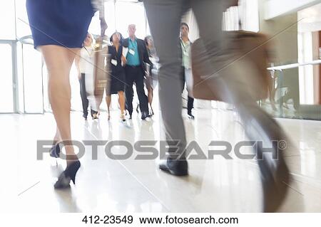 Stock Photo - Legs of businesswoman and businessman carrying hand luggage walking through lobby of conference center. Fotosearch