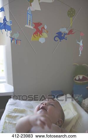 Stock Image - Little baby lying down and looking at colorful hanging mobile. Fotosearch