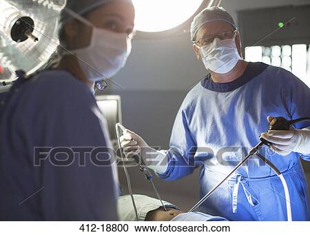 Stock Image - Male and female doctors performing laparoscopic surgery in operating theater. Fotosearch