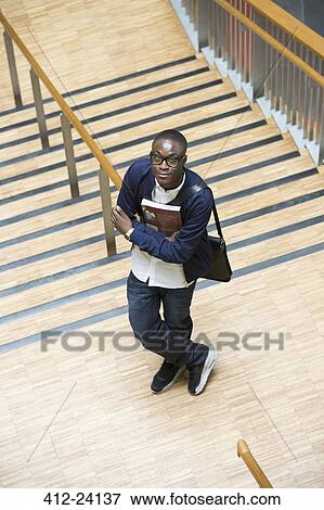 Male student holding books and standing in corridor View Large Photo Image Stock Photo - Male student holding books and standing in corridor. Fotosearch