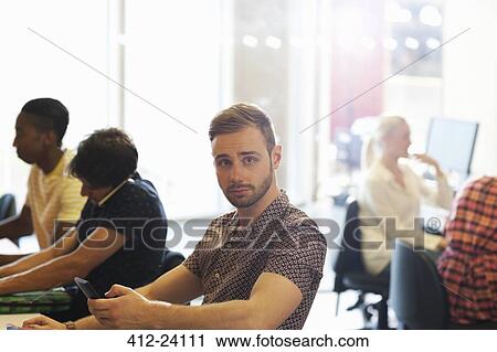 Male student sitting at desk in classroom and using cell phone View Large Photo Image Stock Image - Male student sitting at desk in classroom and using cell phone. Fotosearch