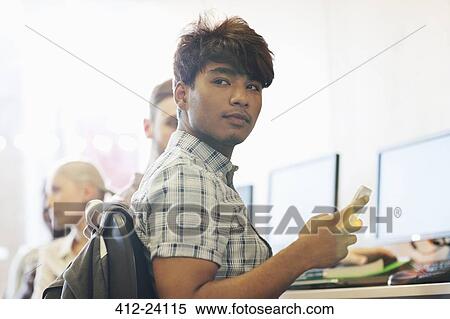 Stock Photography - Male student sitting at desk using cell phone. Fotosearch