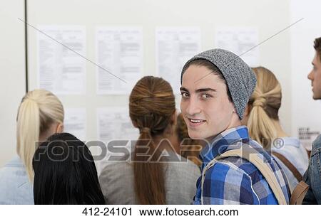 Male student smiling at camera while others read notice board View Large Photo Image Stock Image - Male student smiling at camera while others read notice board. Fotosearch