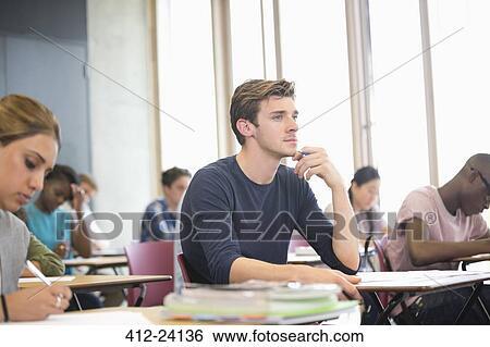 Male student with hand on chin during lecture with other students in background View Large Photo Image Stock Photograph - Male student with hand on chin during lecture with other students in background. Fotosearch