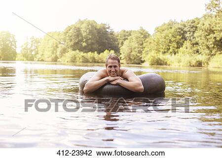 Stock Image - Man floating in inner tube in lake. Fotosearch