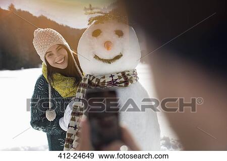 Man photographing woman with snowman View Large Photo Image Stock Photo - Man photographing woman with snowman. Fotosearch