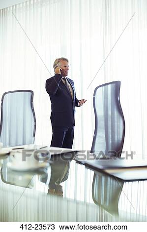 Man standing in conference room talking on his mobile phone View Large Photo Image Stock Image - Man standing in conference room talking on his mobile phone. Fotosearch