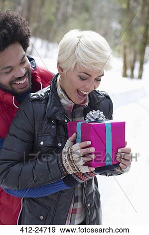 Man surprising woman with Christmas gift in snow View Large Photo Image Stock Photo - Man surprising woman with Christmas gift in snow. Fotosearch