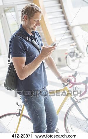 Man using cell phone and holding bicycle View Large Photo Image Stock Image - Man using cell phone and holding bicycle. Fotosearch