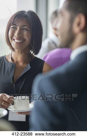 Stock Photo - Mature woman with coffee cup talking to people during seminar break. Fotosearch