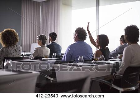 Stock Image - Medium group of conference participants sitting in conference room with woman raising hand. Fotosearch