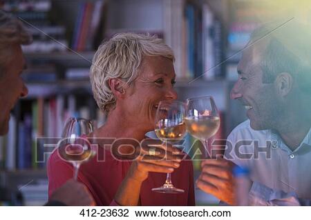 Stock Image - Older friends toasting each other with white wine. Fotosearch