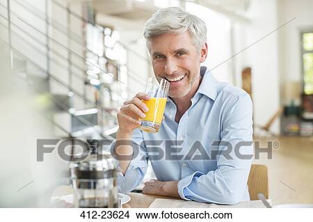 Picture - Older man drinking orange juice at breakfast table. Fotosearch