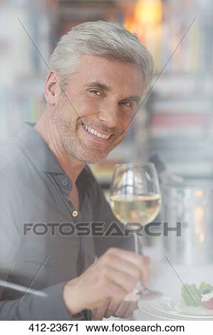 Stock Image - Older man drinking white wine at dinner. Fotosearch