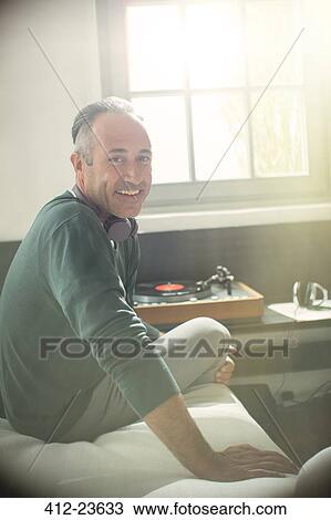 Stock Image - Older man listening to record player with headphones. Fotosearch