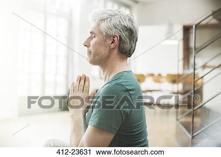 Stock Image - Older man meditating indoors. Fotosearch