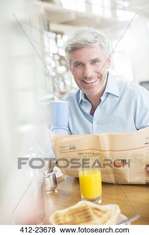Older man reading newspaper at breakfast table View Large Photo Image Stock Photo - Older man reading newspaper at breakfast table. Fotosearch