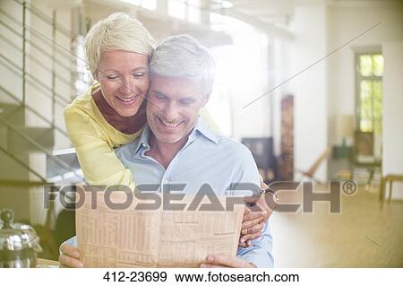 Older woman hugging husband reading newspaper View Large Photo Image Stock Photo - Older woman hugging husband reading newspaper. Fotosearch