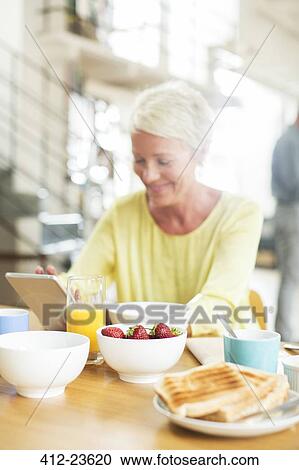 Stock Image - Older woman using digital tablet at breakfast table. Fotosearch