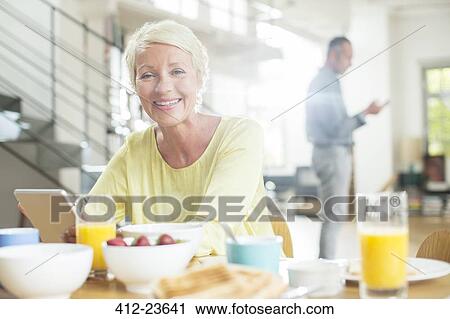 Stock Image - Older woman using digital tablet at breakfast table. Fotosearch