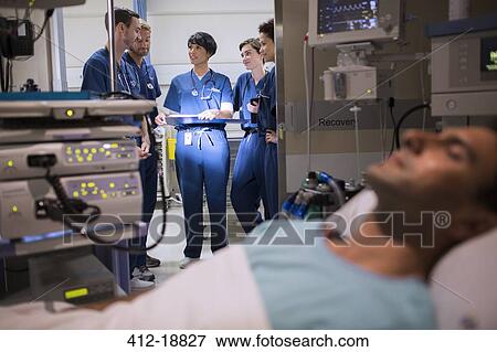 Stock Photo - Patient attached to medical monitoring equipment in intensive care unit, doctors standing in doorway. Fotosearch
