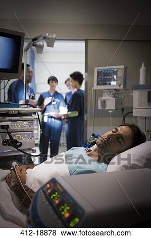 Patient lying in bed in intensive care unit, doctors discussing in background View Large Photo Image Stock Photo - Patient lying in bed in intensive care unit, doctors discussing in background. Fotosearch