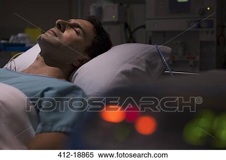 Stock Photography - Patient lying in hospital bed in intensive care unit, medical equipment in foreground. Fotosearch