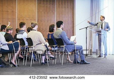 Portrait of businessman standing at transparent lectern talking before audience in conference room View Large Photo Image Stock Image - Portrait of businessman standing at transparent lectern talking before audience in conference room. Fotosearch