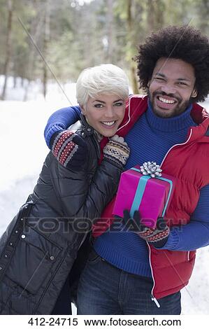 Portrait of couple with Christmas gift hugging in snow View Large Photo Image Stock Photography - Portrait of couple with Christmas gift hugging in snow. Fotosearch