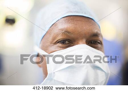 Stock Image - Portrait of doctor wearing surgical cap and mask in operating theater. Fotosearch