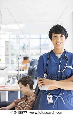 Stock Photo - Portrait of doctor with arms crossed, patient undergoing medical treatment in background. Fotosearch